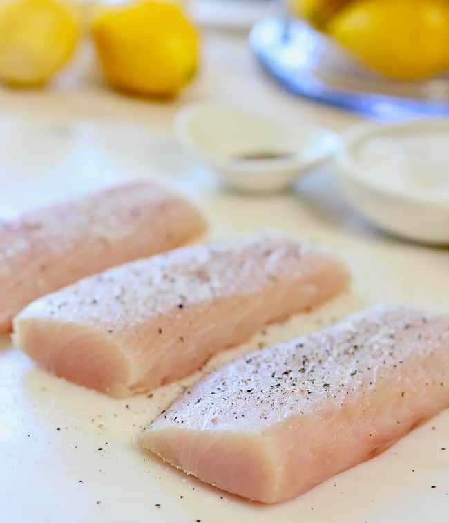 Fresh fish fillets being sprinkled with salt and pepper