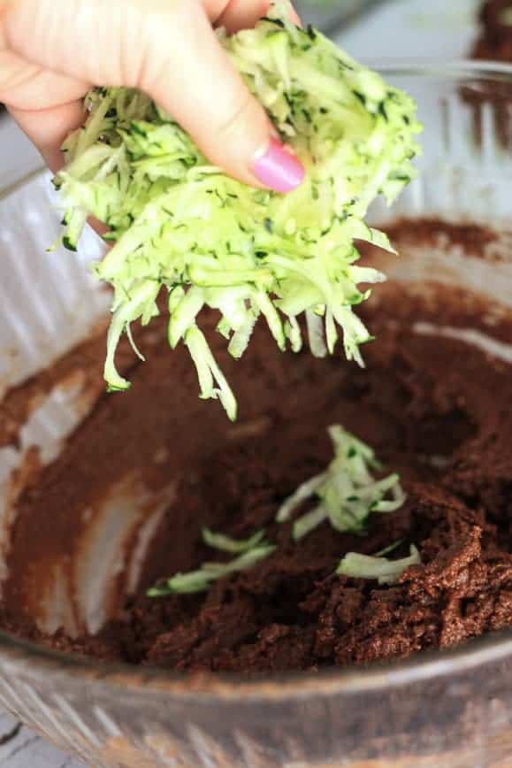 a handful of shredded zucchini being poured into a bowl of chocolate cake mixture