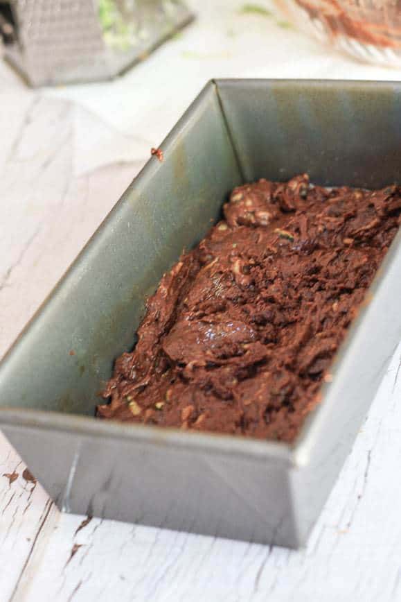 A loaf pan on a light wooden table filled with chocolate zucchini batter