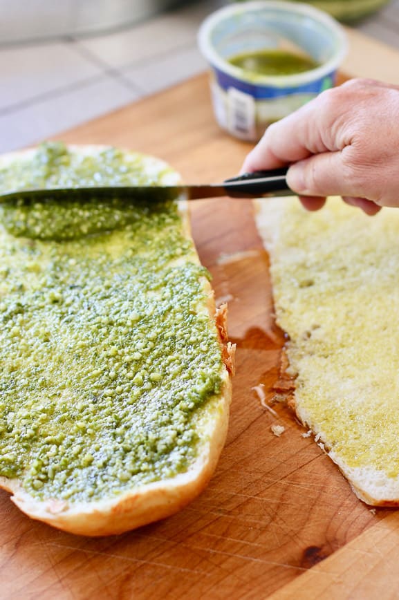 spreading pesto and olive oil on foccocia bread