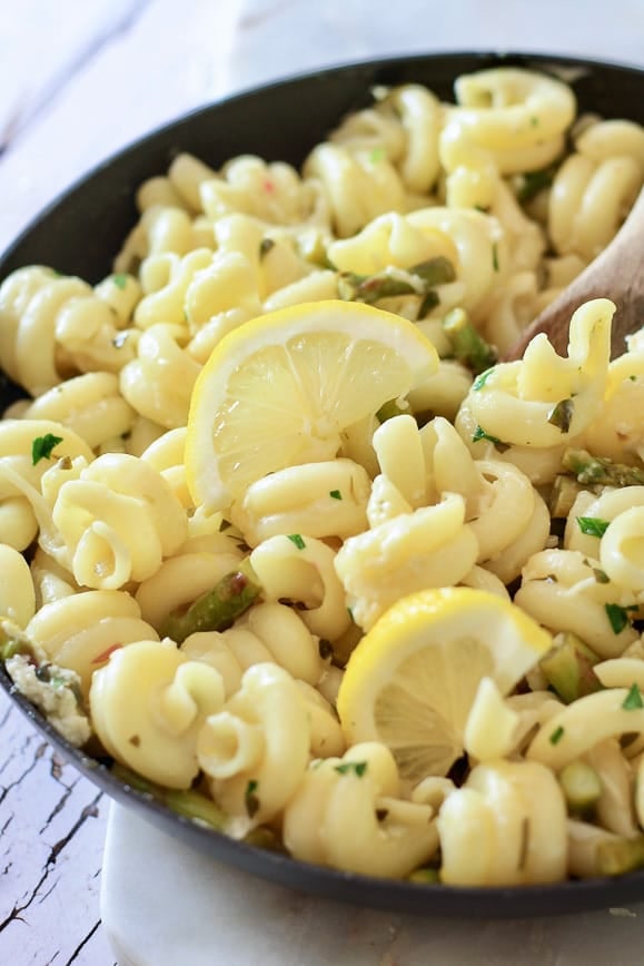 A black skillet with cavatappi and asparagus garnished with lemon slices and parsley