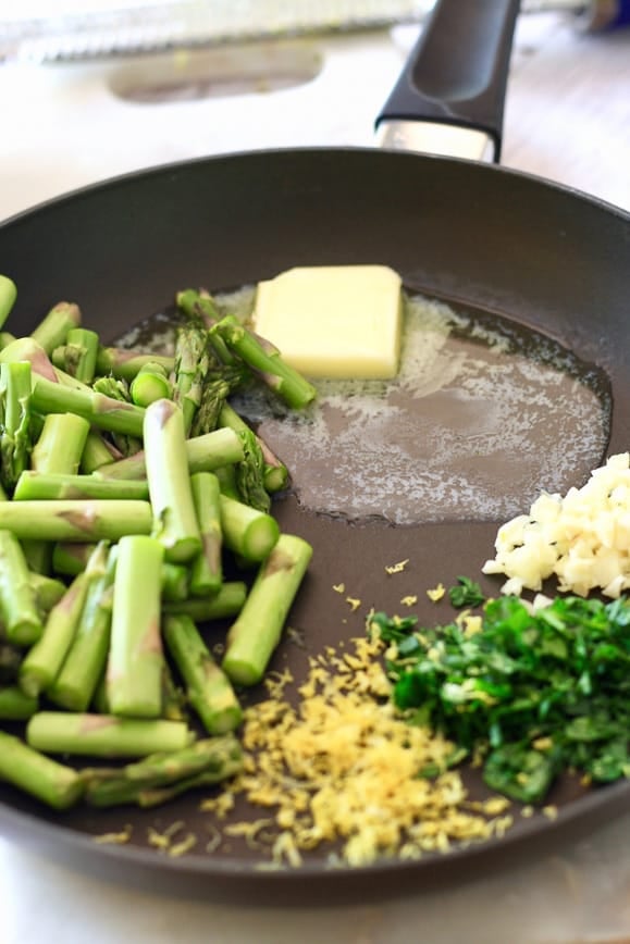 a black skillet with butter melted, parley, garlic, lemon zest and asparagus