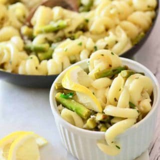 a white bowl filled with cavatapi pasta asparagus and slices of lemon