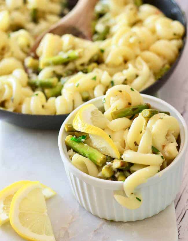 a white bowl filled with cavatapi pasta asparagus and slices of lemon
