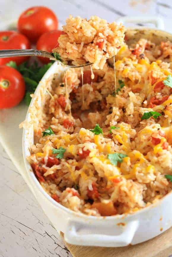 A white dish with tomatoes in the background filled with Mexican rice topped with cheese and cilantro