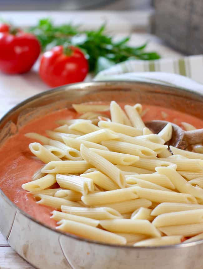 pasta and cream sauce being combined in skillet