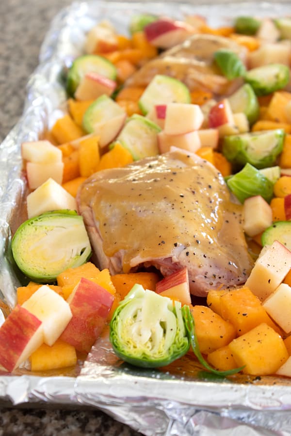 raw chicken with veggies and apples on a sheet pan