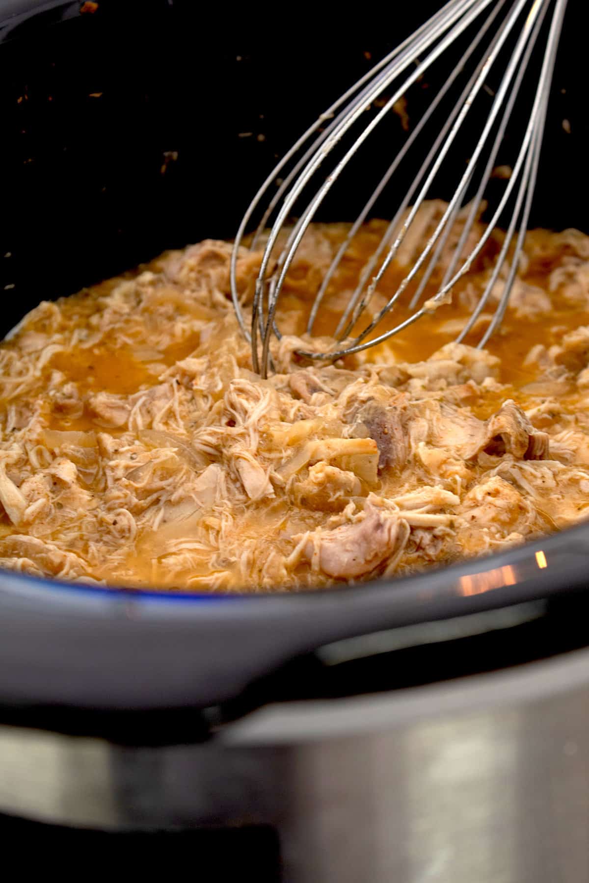 shredding chicken with a whisk in a slow cooker