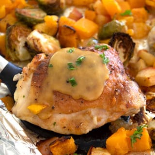 sheet pan with a spatula holding chicken amidst butternut squash bruseel sprouts and apples
