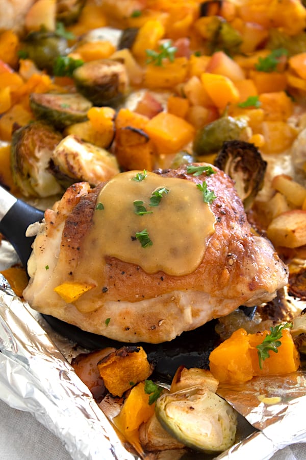 sheet pan with a spatula holding chicken amidst butternut squash bruseel sprouts and apples
