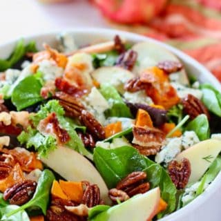 fall salad in a white serving bowl with apples in background