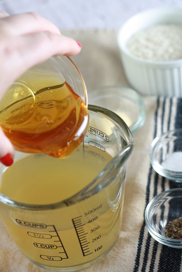 a clear 2 cup measuring cup filled to the 400ml line with chicken broth and honey being poured into it