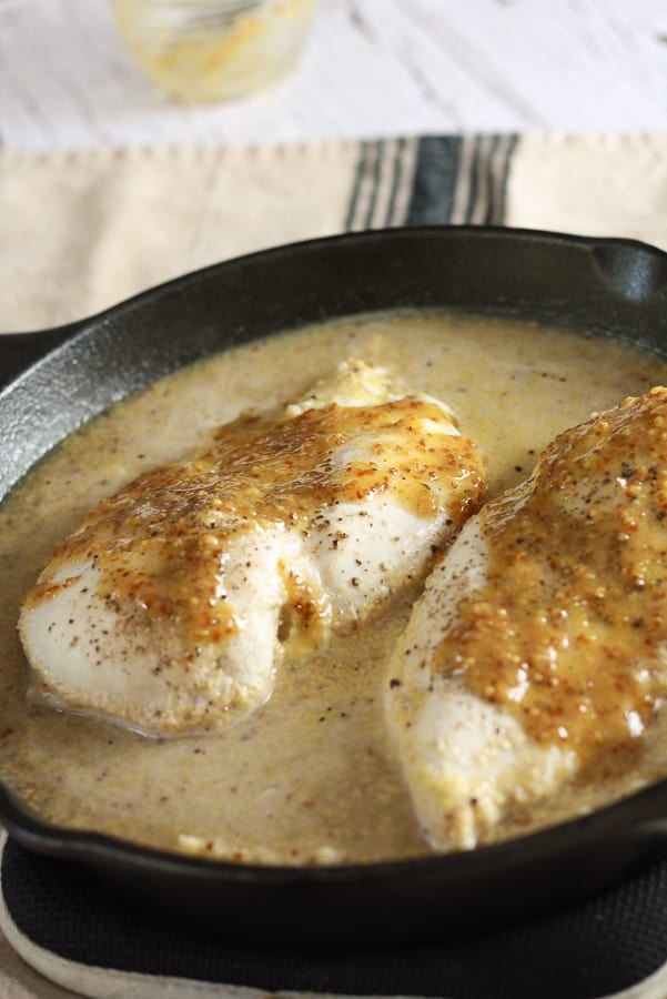 A black cast iron pan with a watery mixture of rice, broth, and 2 chicken breasts slathered in honey mustard sauce