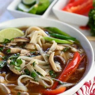 Noodles and broth in a beautiful white bowl topped with veggies for an amazing chicken pho