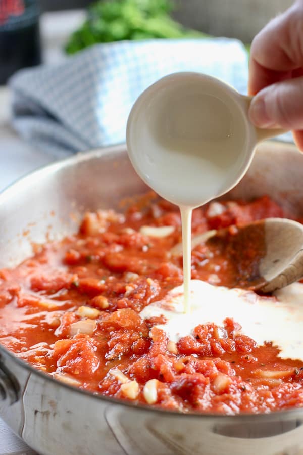 cream being poured into tomato sauce in skillet
