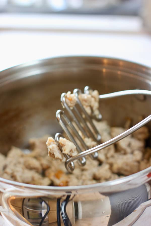 ground turkey being browned in a large pot and stirred with a potato masher