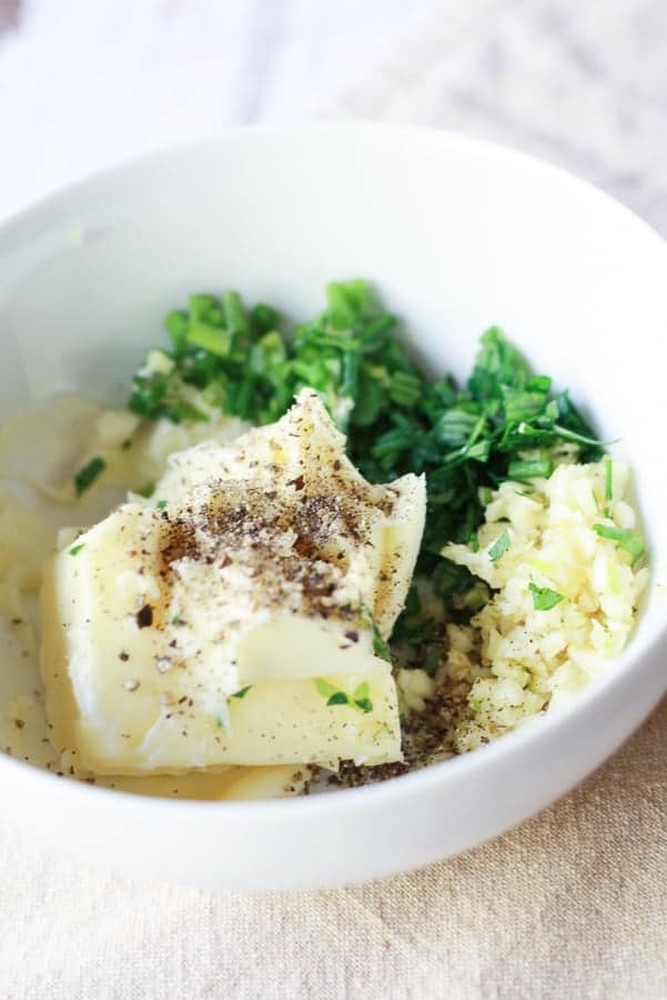 compound butter ingredients in white bowl- butter, garlic, parsley, and salt and pepper