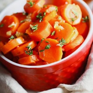 candied carrots in a red bowl with thyme and garlic