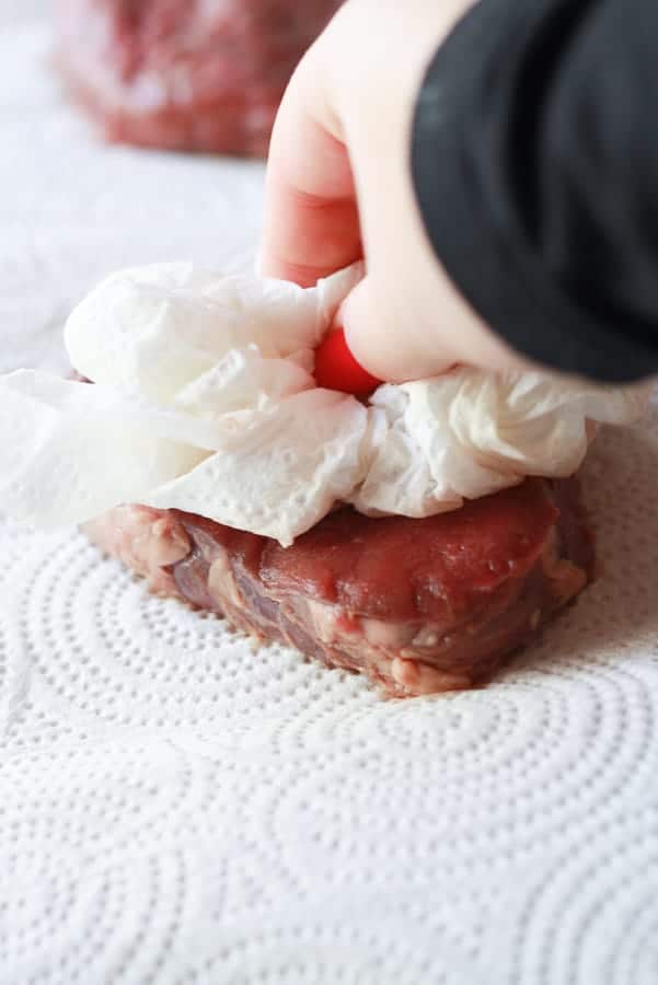 steak being dabbed with paper towel to remove excess moisture