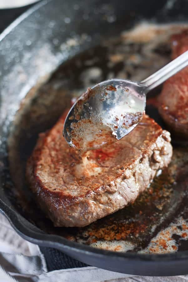spooning butter onto steak in cast iron pan