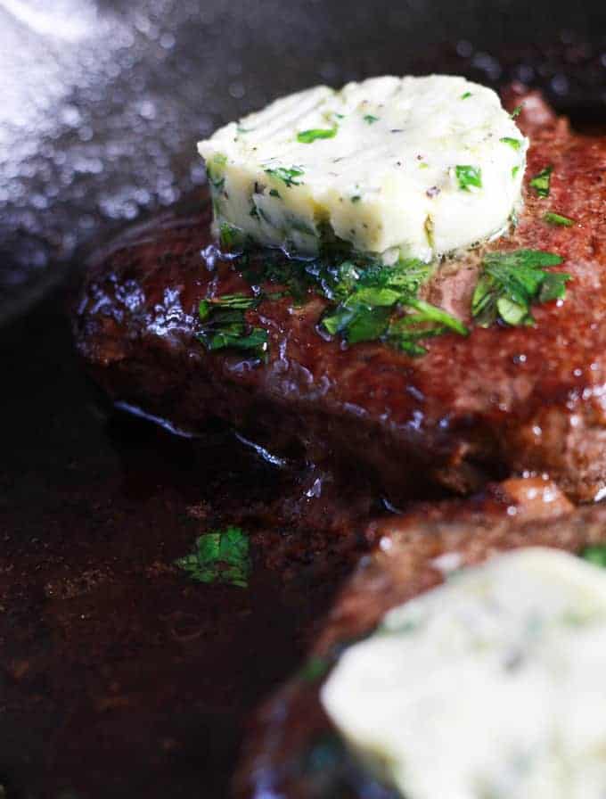 highlighting steak with compound butter in cast iron pan garnished with parsley