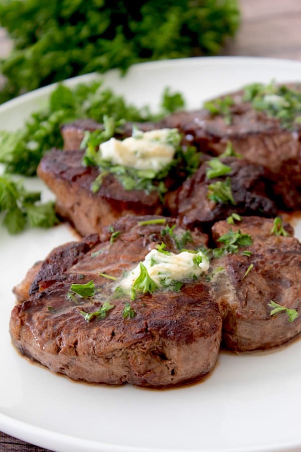cooked steak on a white platter with compound butter and parsley garnish