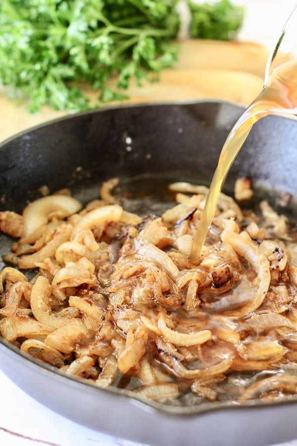 carmalized onions in a cast iron skillet with broth being poured