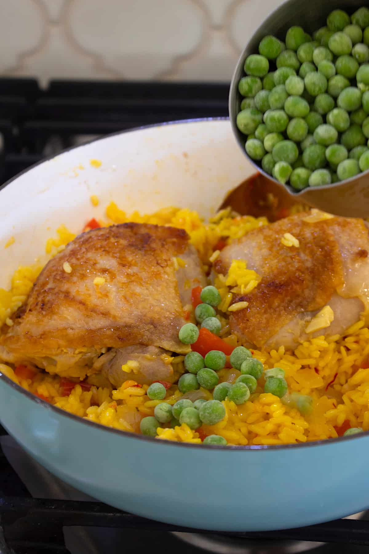 adding frozen peas to pan with chicken and rice