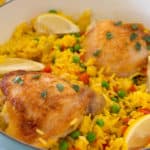 white ceramic pan full of arroz con pollo garnished with lemon wedges