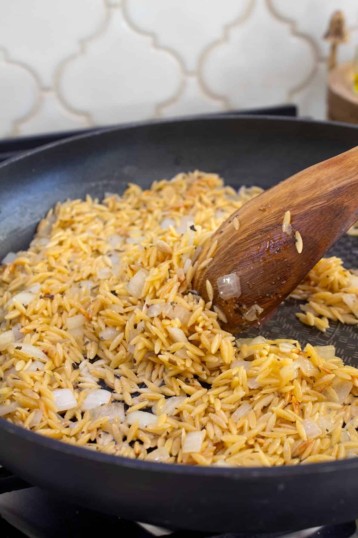 cooking orzo and onion in a black pot