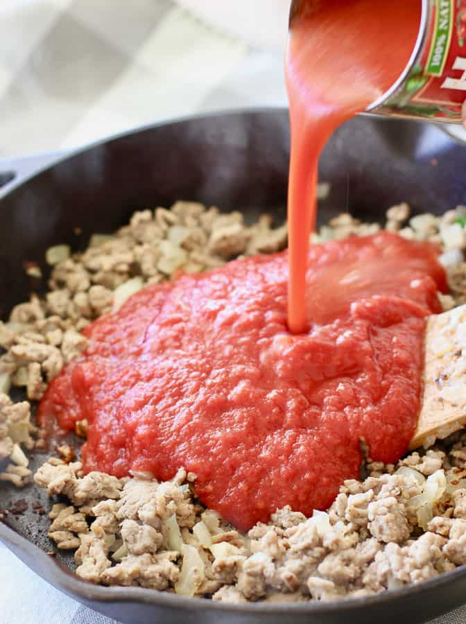 tomato puree being poured over cooked ground turkey