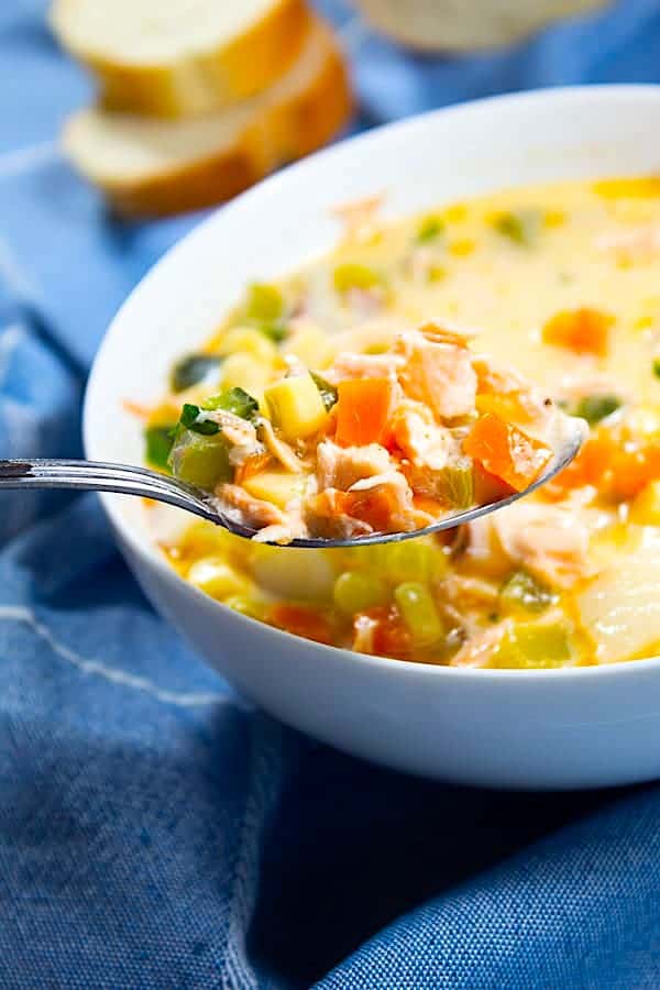 salmon chowder on a spoon with a white bowl of chowder in background