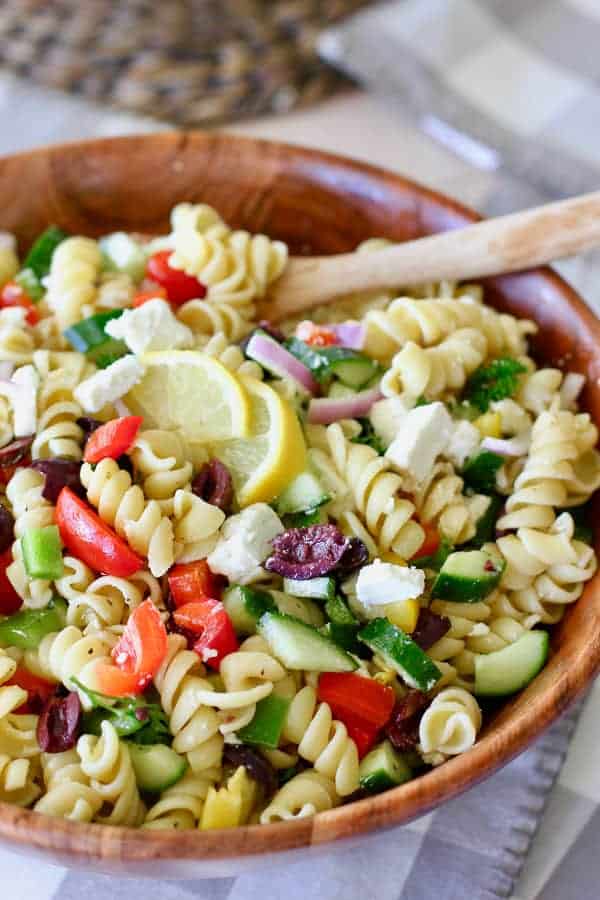 greek pasta salad being served in a wooden bowl