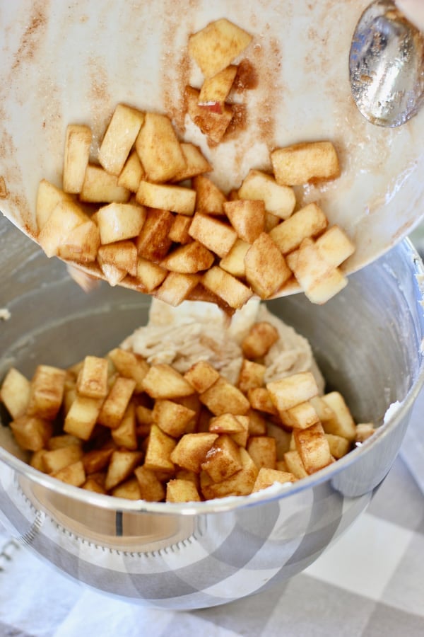 pouring diced apples into apple cake mixture