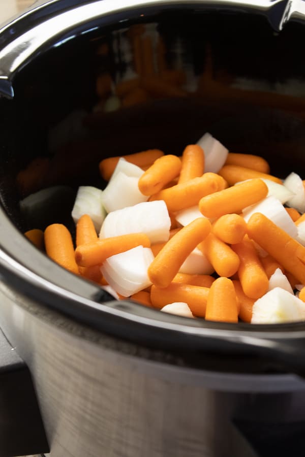 a slow cooker with raw carrots and onions inside 