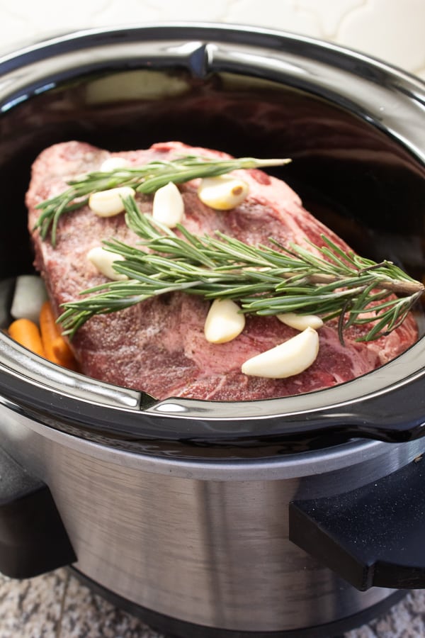 a pot roast in a slow cooker with fresh garlic and rosemary 