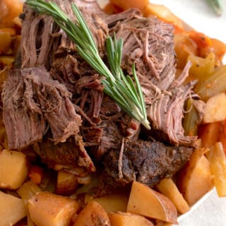 pot roast on a white plate with potatoes and rosemary garnish