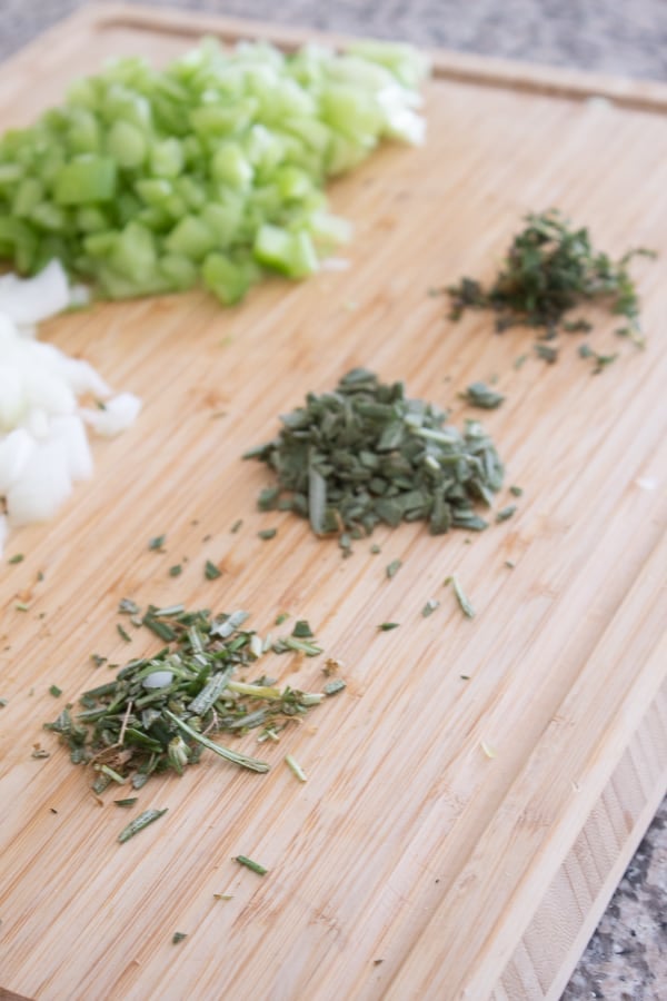 Chopped onion celery and herbs on a bamboo cutting board