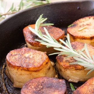 fondant potatoes with rosemary garnish in a cast iron skillet