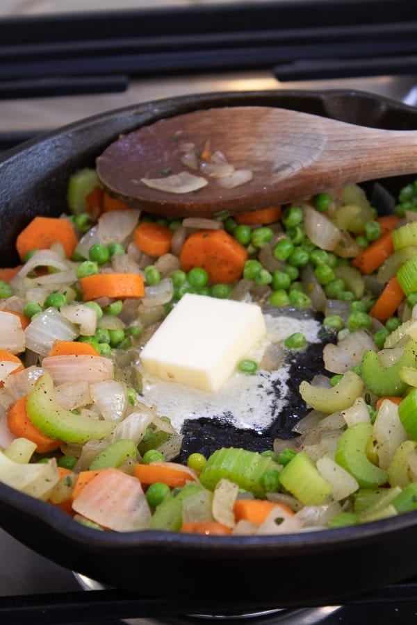 adding butter to chicken pot pie mirepoix in a cast iron skillet