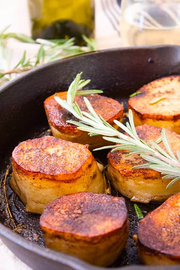 fondant potatoes in a cast iron skillet with a sprig of rosemary for garnish