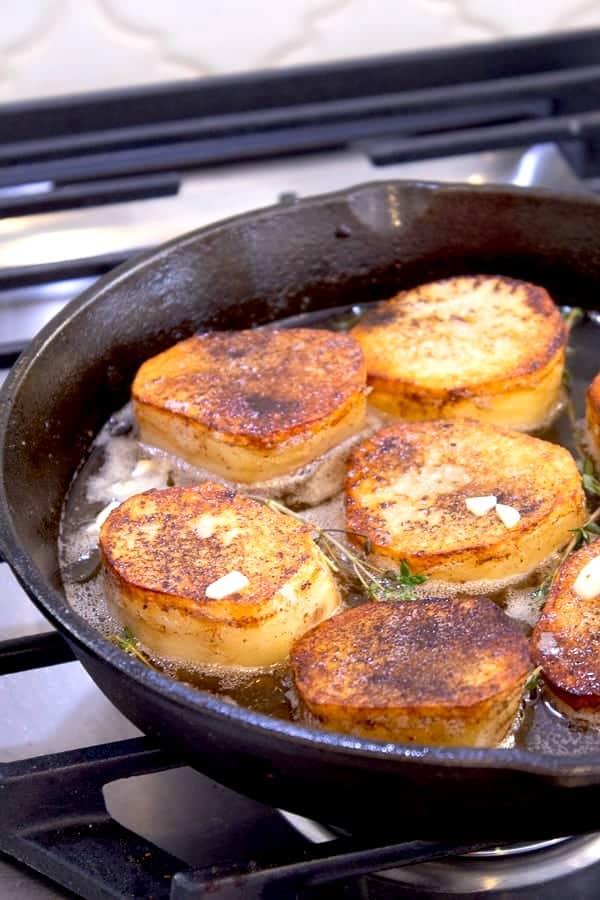 showing fondant potatoes cooking cast iron skillet with wine