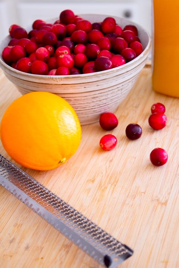 zesting orange with bowl of cranberries cutting board