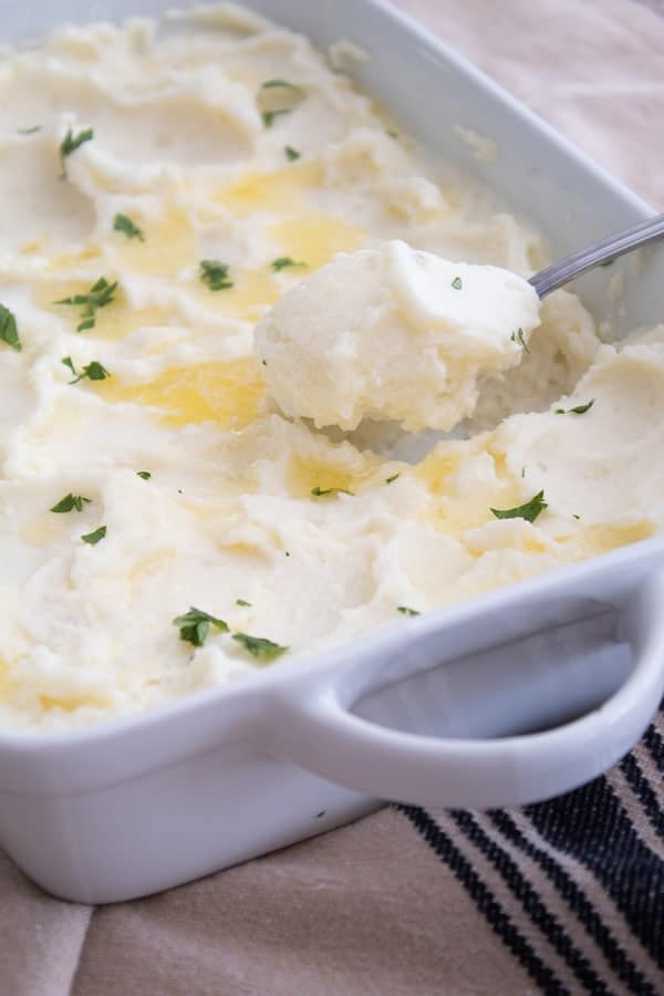 A casserole dish with whipped mashed potatoes topped with butter and parsley