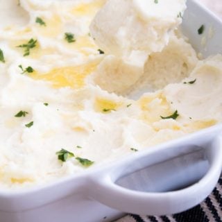 A casserole dish with whipped mashed potatoes topped with butter and parsley