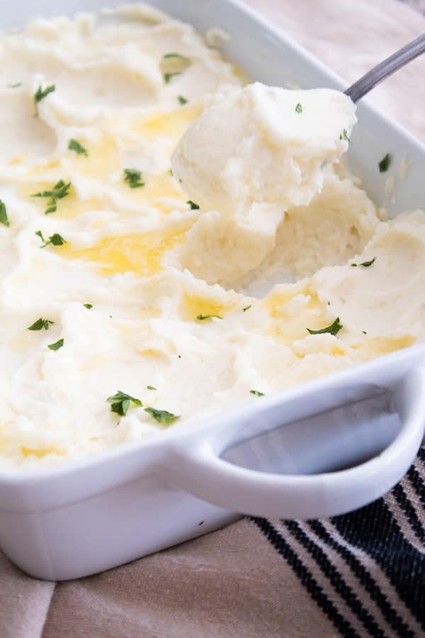A casserole dish with whipped mashed potatoes topped with butter and parsley