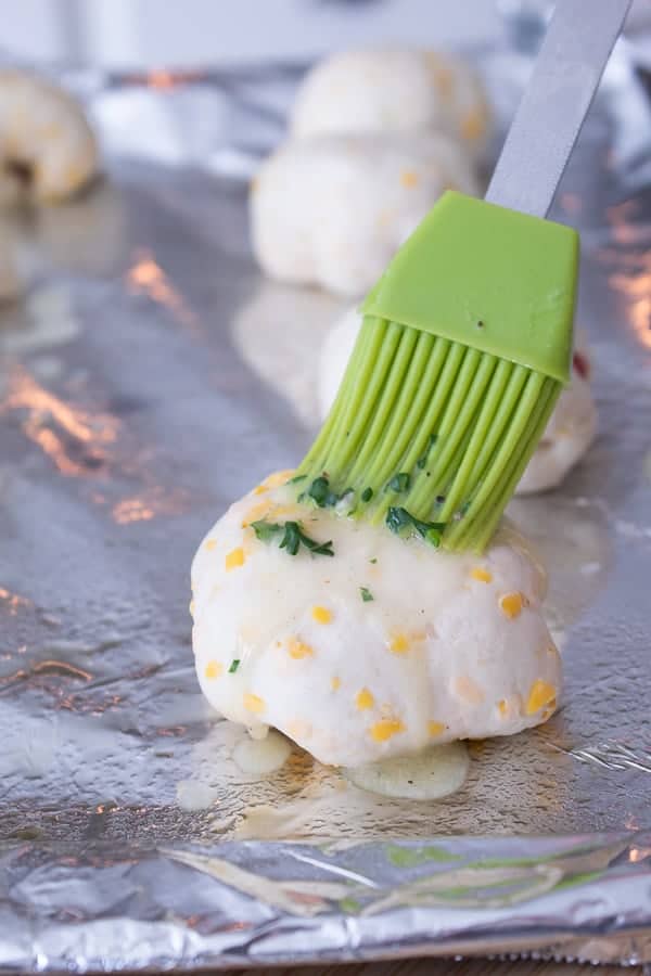 brushing brie and cranberry stuffed raw biscuit bomb with garlic butter