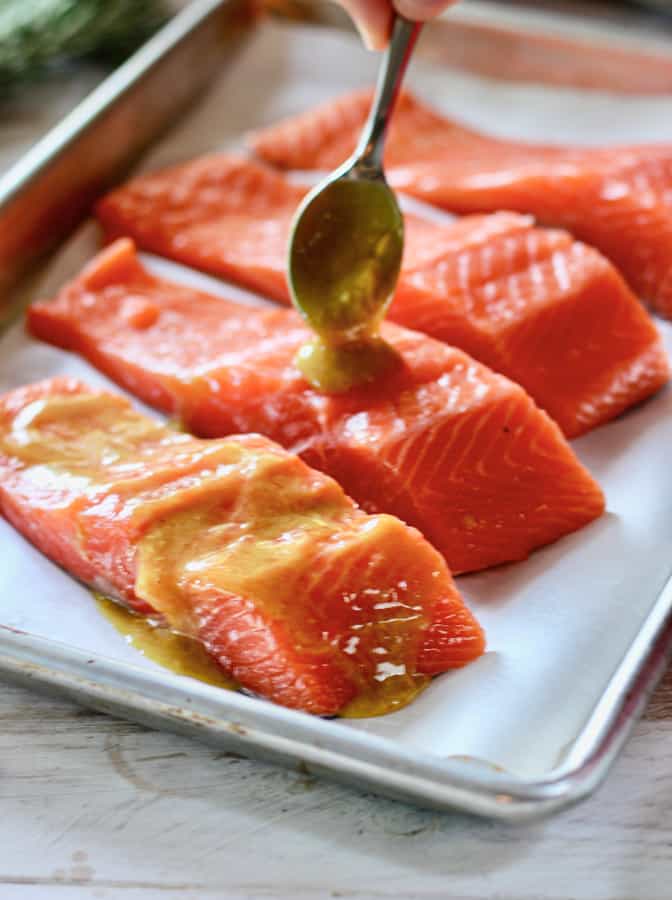 dijon and butter being brushed on to salmon fillets