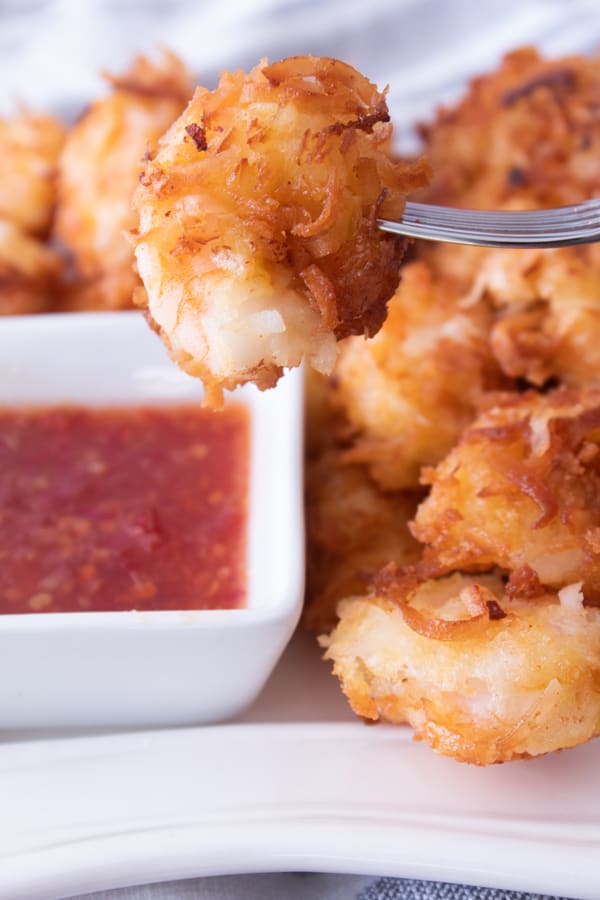 coconut shrimp on a silver fork with chili sauce in the background