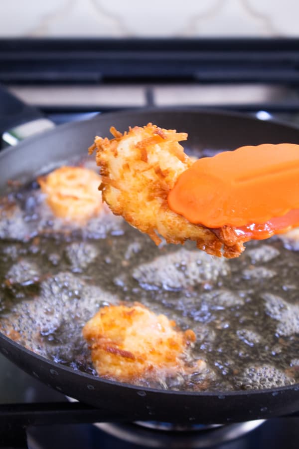frying coconut shrimp in a shallow black pan